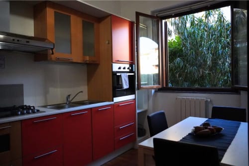 Cucina moderna con mobili rossi e dettagli in legno, tavolo da pranzo, vista sul giardino, Roma 2 Apartment della collezione THE V