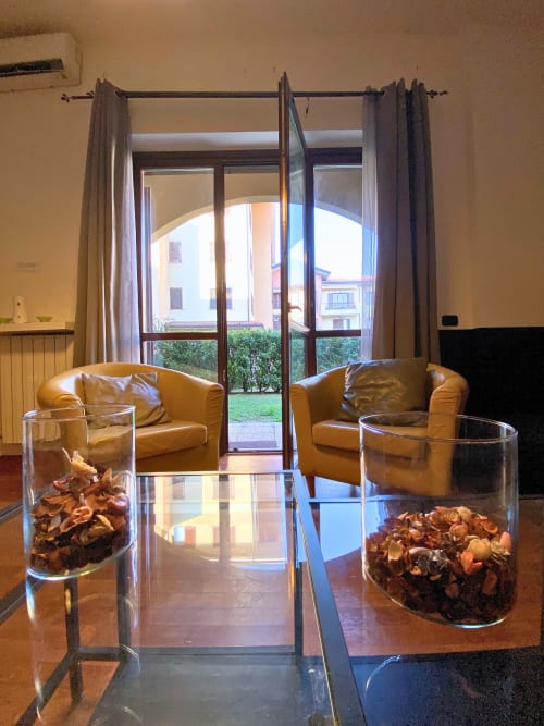 Elegante soggiorno dell'appartamento Roma 2 con poltrone in pelle, tavolo in vetro e vista giardino attraverso le porte finestre presso THE V