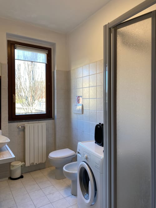 Bagno moderno nell'Appartamento Roma 2 con toilet, lavatrice, doccia e finestra presso THE V Collection a Turate
