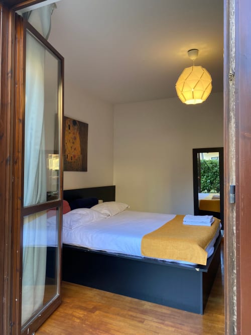 Camera moderna nell'Appartamento Roma 2 di THE V Collection, Turate, con letto nero, lampada a sospensione gialla e porta con vista giardino