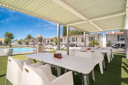 Outdoor dining area under pergola at Bungalow Buda Beach in Chipiona with pool and garden view