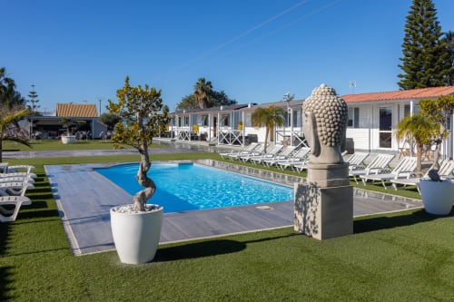 Bungalow Buda Beach pool area in Chipiona with loungers, Buddha statue, and white bungalows