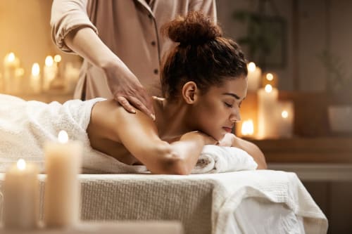 Femme recevant un massage relaxant du dos par une thérapeute dans une salle de spa à la lumière des bougies aux Secrets de Winna