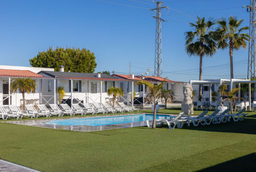 Bungalow Buda Beach pool and garden area in Chipiona with lounge chairs and white bungalows