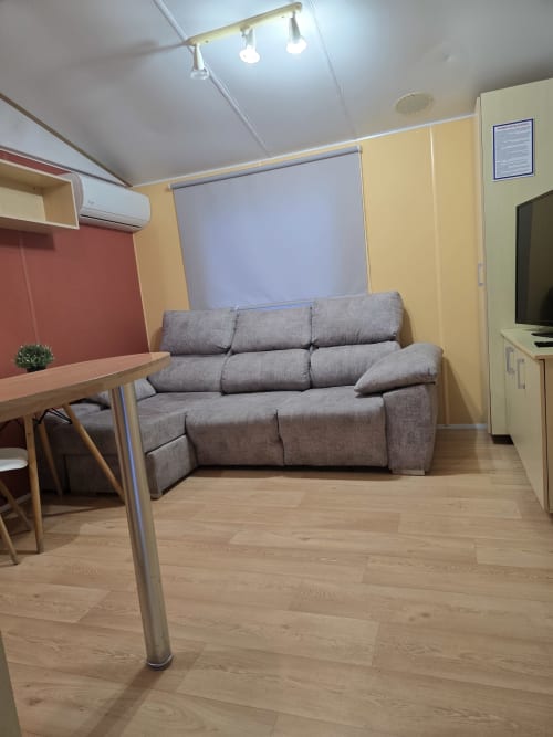 Modern living area in Bungalow G at Buda Beach hotel, Chipiona, with gray sofa, dining table, and equipped kitchen