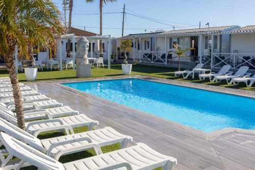Bungalow Buda Beach pool area in Chipiona with white loungers, palm tree, and modern bungalows