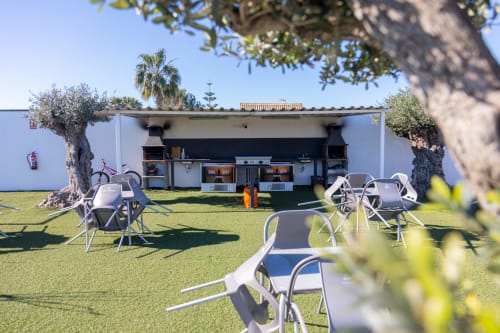 Bungalow Buda Beach garden with outdoor seating, olive trees, and beachfront pavilion in Chipiona