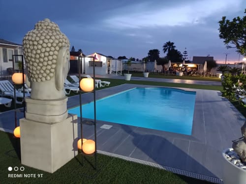 Piscina Bungalow Buda Beach al atardecer con estatua de Buda iluminada, tumbonas y jardines verdes en Chipiona