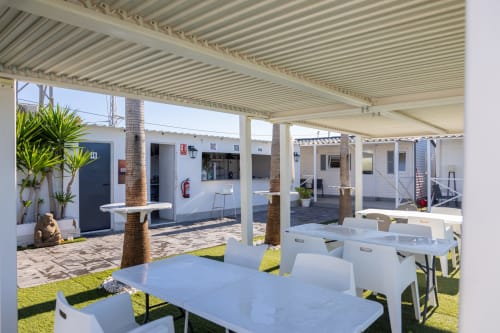 Outdoor courtyard at Bungalow Buda Beach with white tables, palm trees, and covered pergola seating area in Chipiona