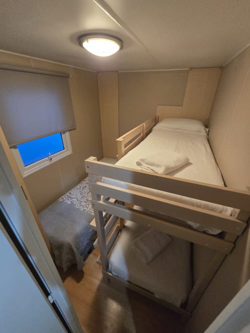 Compact bungalow bedroom at Bungalow Buda Beach with bunk beds, overhead light, window with blue view, wooden furnishings,
