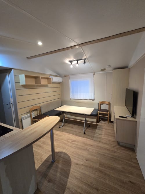 Modern bungalow interior at Buda Beach Chipiona with dining table, sofa bed, TV, kitchen, and storage shelving