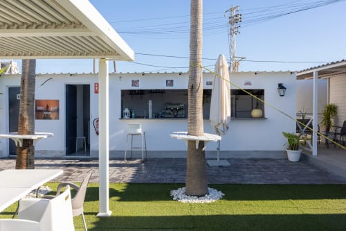 Bungalow Buda Beach terrace in Chipiona with palm trees, white umbrellas, and garden seating area