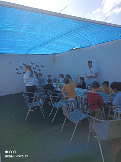 Children's outdoor event under blue shade at Bungalow Buda Beach hotel in Chipiona with tables, chairs and activity leaders