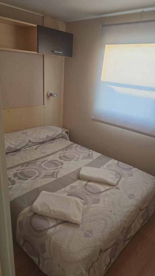 Cozy bedroom in Bungalow J at Buda Beach hotel, Chipiona, with double bed, white pillows, patterned bedding, wall-mounted TV,