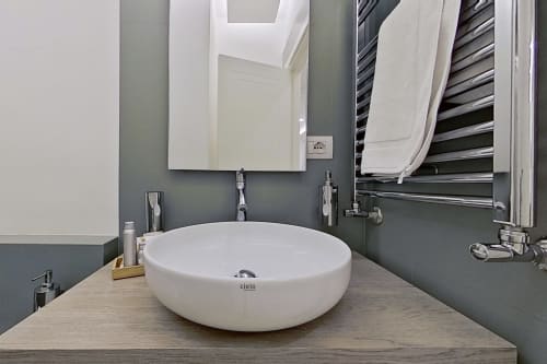 Lavabo moderno dell'hotel Museo19 di Napoli con lavabo tondo bianco, pareti grigie, specchio e scaldasalviette elettrico