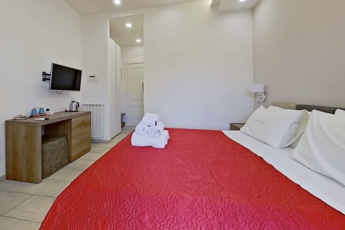 Moderna habitación doble en Museo19 B&B en Nápoles con colcha roja, escritorio de madera, TV en pared y decoración minimalista blanca