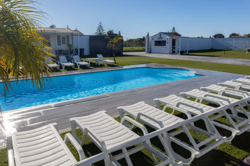 Bungalow Buda Beach pool area in Chipiona with loungers, palm trees, and beachfront bungalows