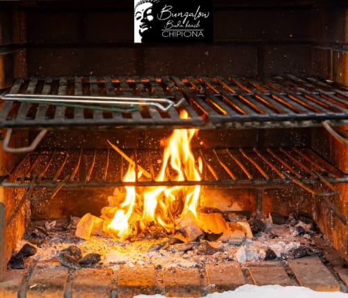 Wood-fired grill at Bungalow Buda Beach restaurant in Chipiona with flames and hot coals ready for cooking