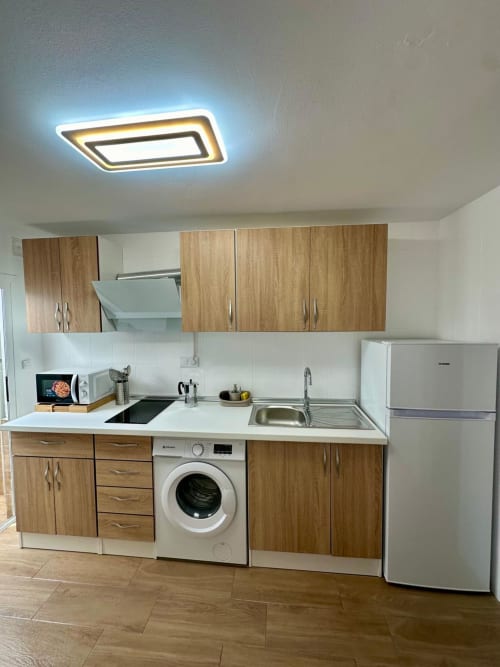 Cocina moderna con muebles de madera, lavadora, estufa, fregadero y refrigerador blanco en apartamento de Mérida