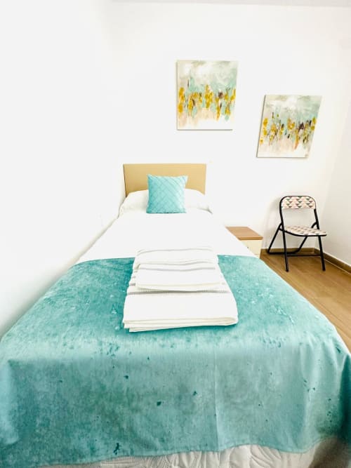 Luminosa habitación de apartamento en Mérida con ropa de cama turquesa, cabecera amarilla y arte mural abstracto