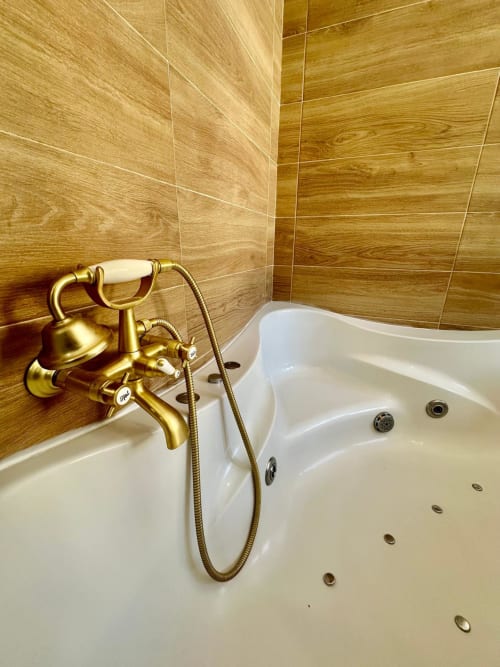 Baño de lujo en apartamento de Mérida con grifo vintage dorado, bañera jacuzzi blanca y paredes con azulejos efecto madera.