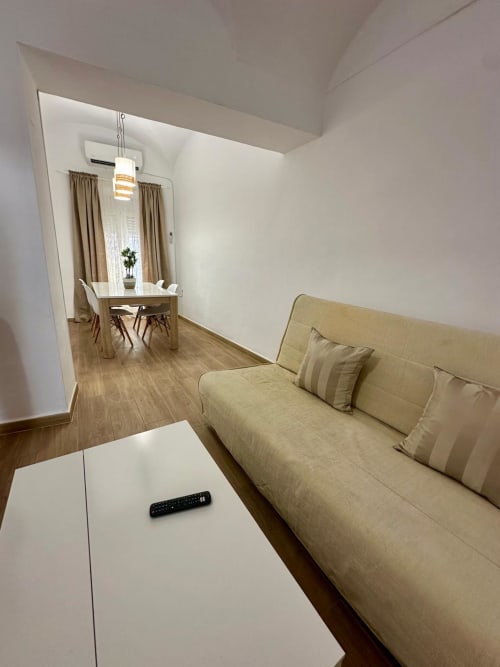 Sala de estar moderna en Mérida con sofá beis, mesa de café blanca y comedor visible a través de la puerta abierta