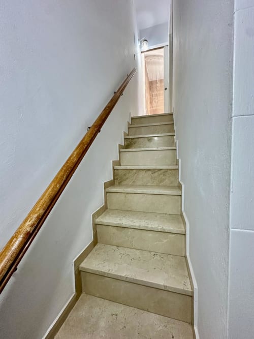Escalera con pasamanos de madera ascendiendo hacia la luz natural, apartamento Gestyp-AT en Mérida