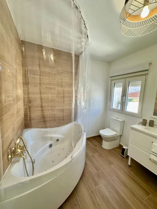 Baño moderno en apartamento Gestyp-AT, Mérida con bañera de hidromasaje esquinera, inodoro y piso estilo madera