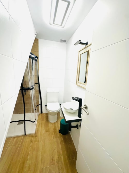 Baño moderno en apartamento Gestyp-AT de Mérida con ducha, inodoro, lavamanos, pisos efecto madera y paredes con azulejos blancos