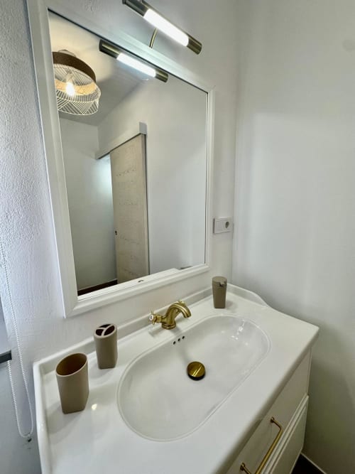 Moderno tocador de baño con lavamanos blanco, grifo dorado y espejo iluminado en apartamento de Mérida