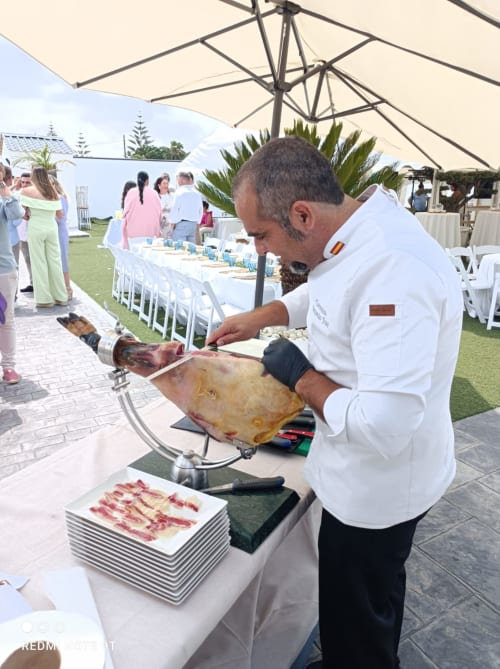 Chef cortando jamón en evento al aire libre bajo sombrillas en Bungalow Buda Beach, Chipiona
