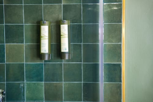 Due flaconi di articoli da toeletta su una parete piastrellata verde nel bagno di Villa Ceci B&B ad Andria, Italia