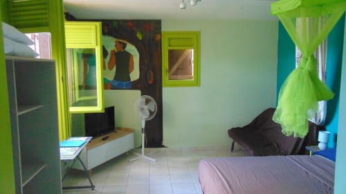 Chambre lumineuse à Caribgites à Sainte-Anne avec accents vert citron, lit, bureau, TV, ventilateur et vue sur le jardin
