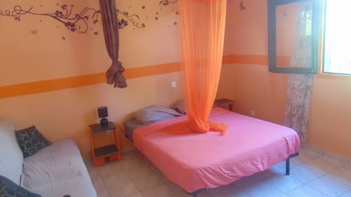 Chambre colorée de la maison d'hôtes Caribgites avec lit rose, rideaux orange et vue sur le jardin à Sainte-Anne