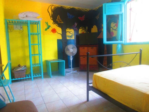 Chambre colorée au Caribgites BnB à Sainte-Anne avec murs jaunes, mobilier turquoise, lit jaune et décoration tropicale