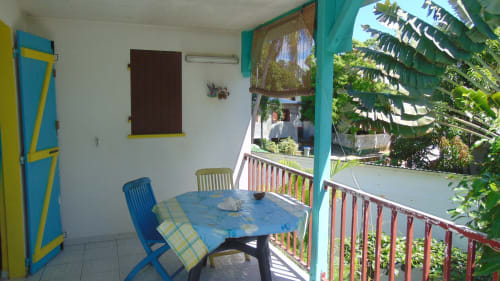 Patio de la maison d'hôtes Caribgites à Sainte-Anne avec table à manger bleue, balustrades turquoise et vue sur le jardin