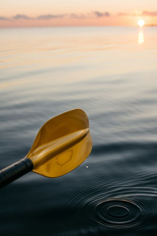 Pagaie jaune créant des ondulations dans l'eau calme au coucher de soleil, Baccara Lodge Arengosse