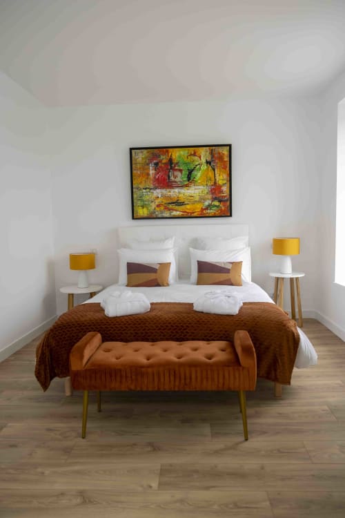 Chambre moderne de l'hôtel Accolade à Châteaudun avec lit blanc, banc ocre, lampes dorées et œuvre d'art abstraite