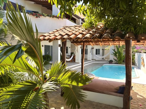Patio de Casa Calilla con piscina privada, pérgola de madera, plantas tropicales y arquitectura de muros blancos en Puerto