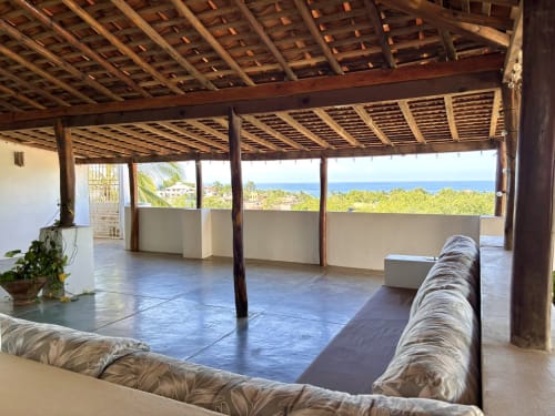 Interior de la cabaña Casa Calilla con vigas de madera, vista al océano y tumbonas frente a Punta Zicatela, Puerto Escondido