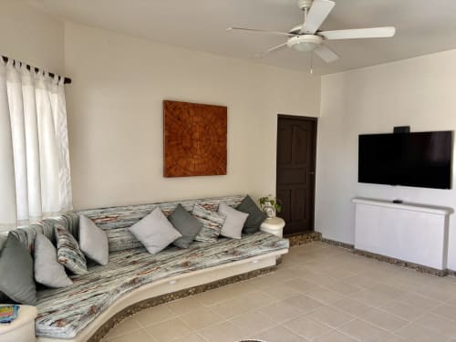 Amplia sala de estar con sofá curvo, TV de pantalla plana, ventilador de techo y arte de madera en Casa Calilla