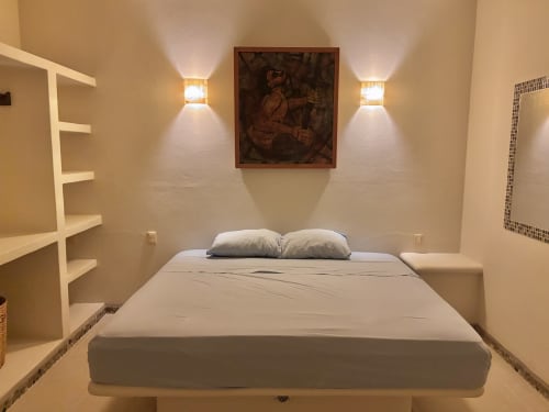 Dormitorio minimalista en la cabaña Calilla & Tsuki, Puerto Escondido, con cama, almohadas blancas, apliques murales y obra de arte