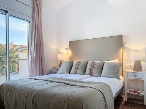 Dormitorio moderno en la casa rural La Bella Lola en L'Estartit con cama tapizada gris, mesillas blancas y acceso a terraza