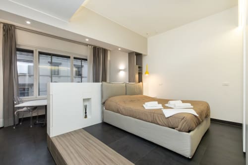 Современная спальня в Magnolia Apartments Милан с бежевой кроватью, белой перегородкой, письменным столом, большими окнами и темным полом