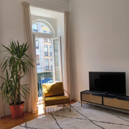 Sala clara do Royal Prince Garden Apartments Lisboa com poltrona amarela, TV, planta e varanda com vista para a cidade