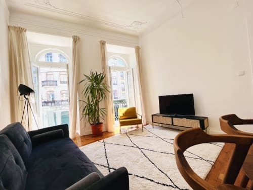 Bright modern living room in Lisbon apartment with black sofa, wooden furniture, TV, plants, and arched windows overlooking