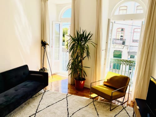 Bright modern living room in Lisboa apartment with black sofa, yellow armchair, potted plant, and garden views through tall