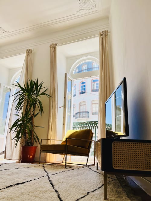 Bright Lisbon apartment with yellow chair, potted plant, flat-screen TV, and city views through French doors with beige