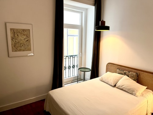 Bright bedroom at Royal Prince Garden Apartments in Lisbon with white bed, rattan headboard, balcony doors, and pendant light