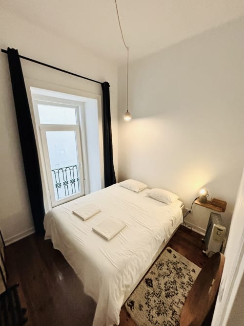 Bright bedroom in Royal Prince Garden Apartments, Lisbon with white bed, black-framed mirror, pendant light, and balcony